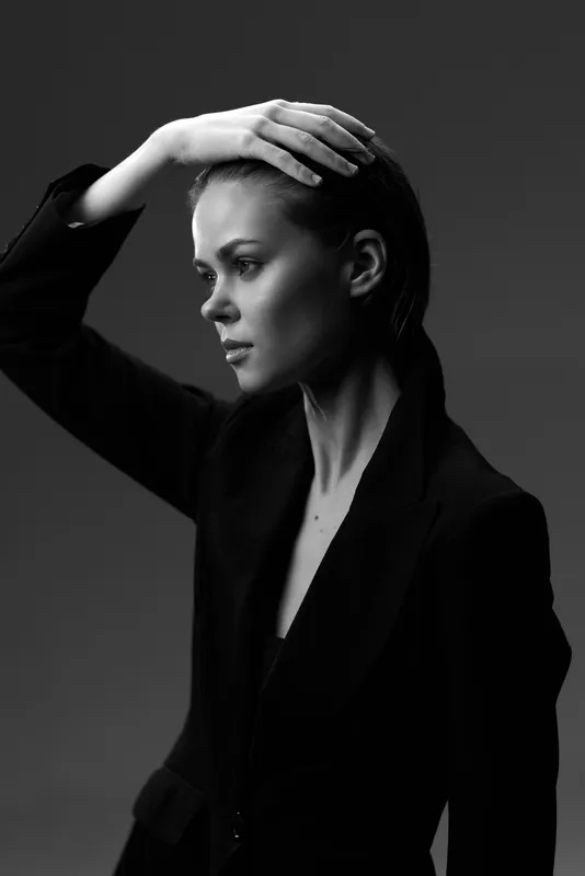Black and white portrait of a pensive woman in a blazer with hand on head, expressing thoughtful emotion and elegance in monochrome style.