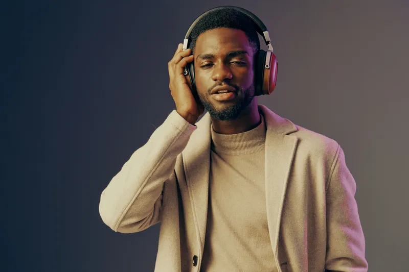 Stylish young black man enjoying music with headphones in a modern setting, showcasing a relaxed expression and contemporary fashion