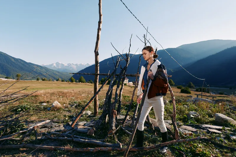 woman hiking with backpack walking through rural meadow near wooden fence with mountains in background, outdoor travel and adventure in nature, scenic landscape and peaceful countryside