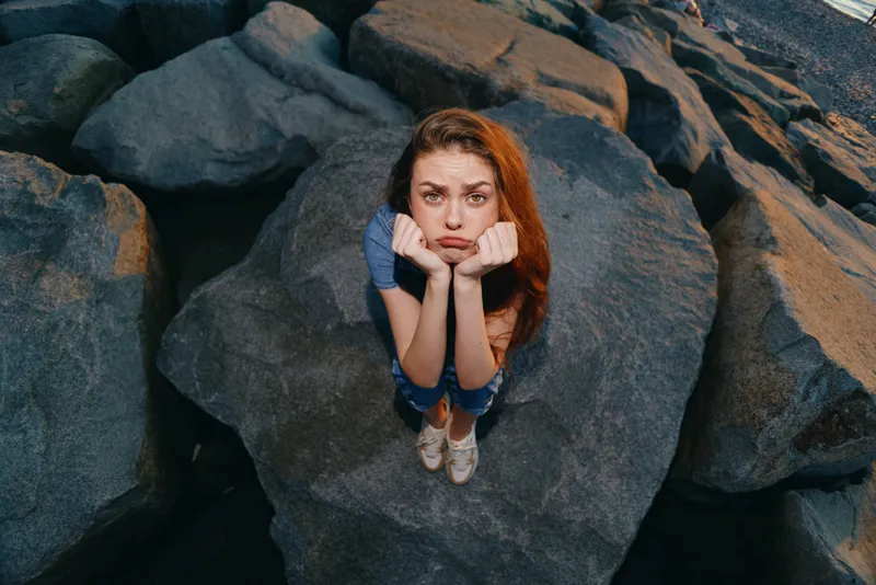 lifestyle woman with modern boho-western denim street style sitting thoughtfully on large rocks, natural light, film color effects capturing mood and texture