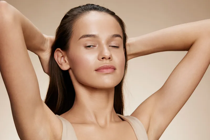 Young woman with smooth skin and a serene expression, showcasing natural beauty, styled hair, and a soft beige background, perfect for skincare and beauty concepts