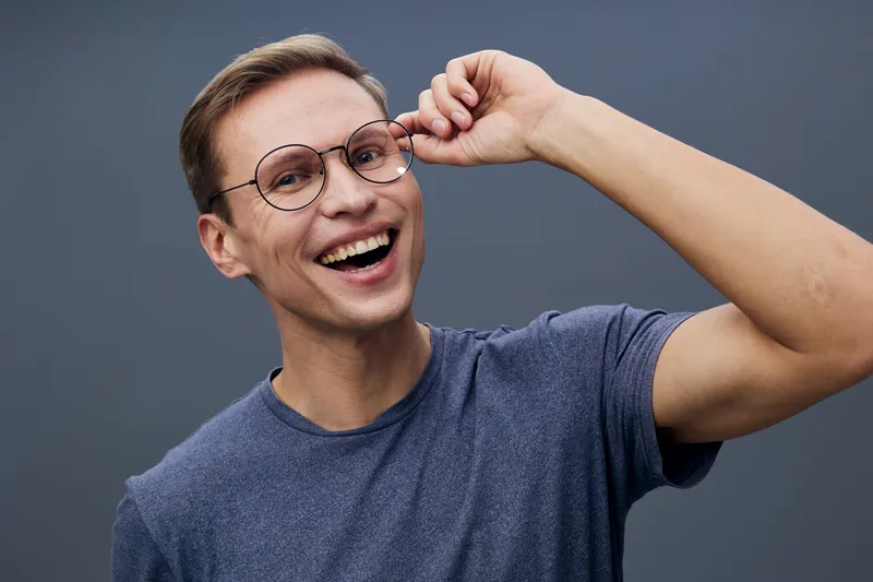 smiling man wearing casual blue t-shirt and round eyeglasses look camera happy cheerful emotional mental health and gadgets concept