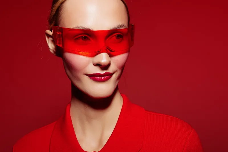 Portrait of a confident woman wearing red sunglasses and a red outfit against a red background. Concept of fashion, style, and bold color contrast in modern photography.