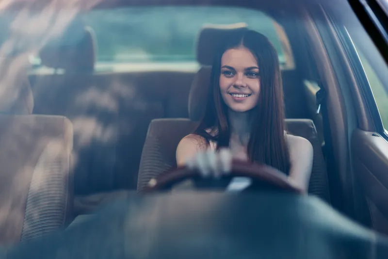 Beautiful young woman smiling while driving a car, showcasing confidence and joy in a summer setting, highlighting a sense of adventure and freedom.