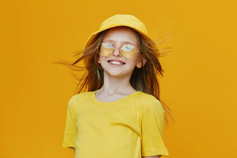 Happy girl in yellow clothing with sunglasses and hat, against a vibrant yellow background, expressing joy and summer vibes, ideal for seasonal marketing or cheerful concepts