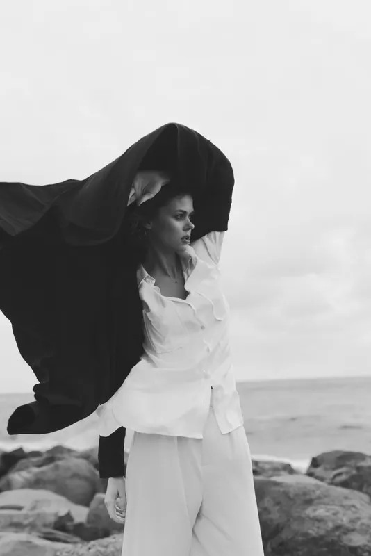 Fashion cloak wind ocean beach scene with flowing garment and dramatic silhouette for a moody artistic edit emphasizing movement and contrast.
