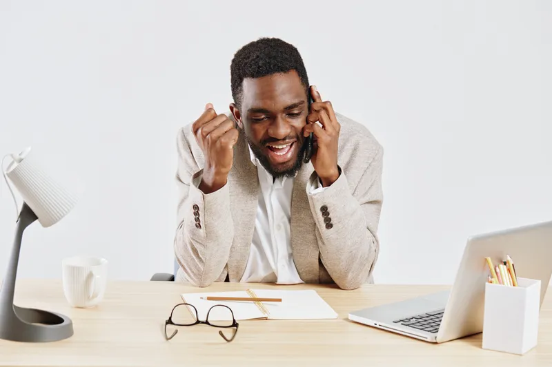 Smiling man working at desk with laptop, glasses, and notepad in a modern office environment, demonstrating productivity, focus, and positive attitude, digital technology, business communication, prof