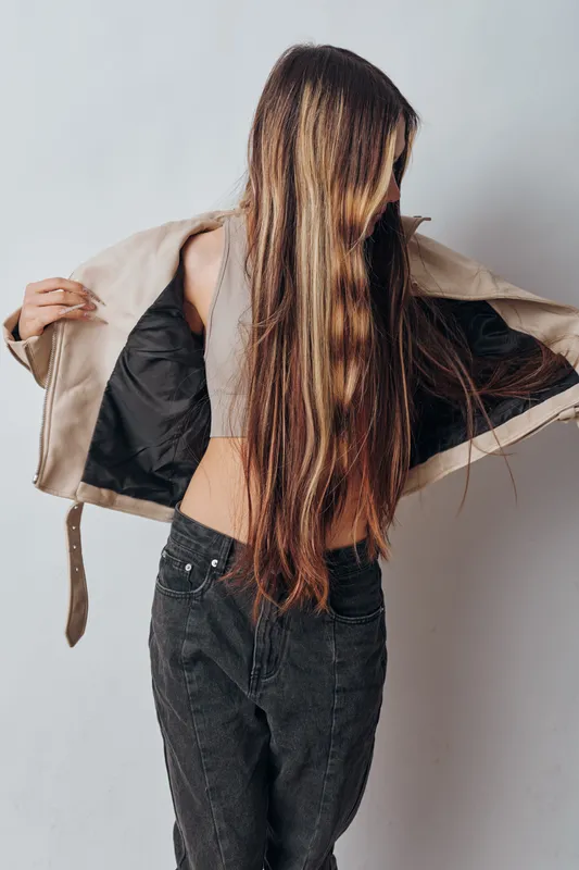 Young woman with long hair wearing a light jacket and casual pants stands against a plain background. Fashion, beauty and casual outfit concept with natural pose and style.