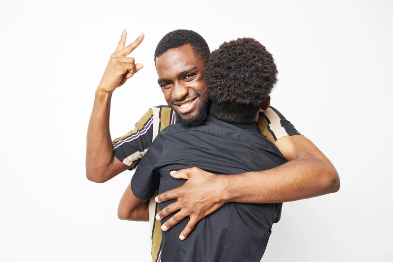 Black man joyfully hugging another individual, showcasing love and connection. Bright colors and playful emotions create a warm, inviting atmosphere.