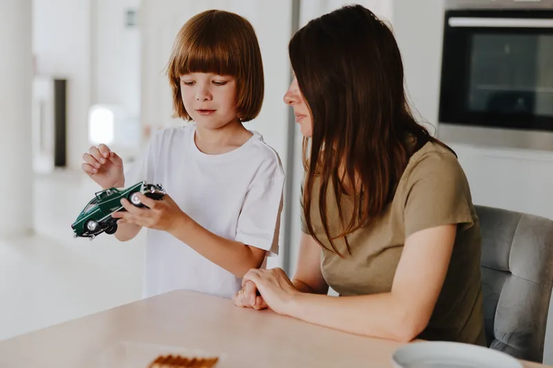 Engaging woman and child interacting, showcasing an educational moment around a toy car, highlighting family bonding and joy in a modern setting.
