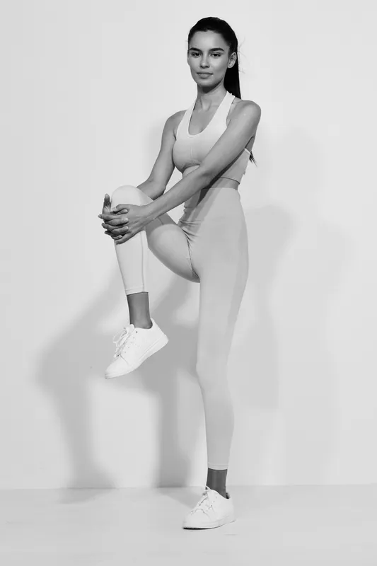 woman sport fitness performing stretching exercise, wearing athletic clothing and sneakers, isolated on light background in black and white