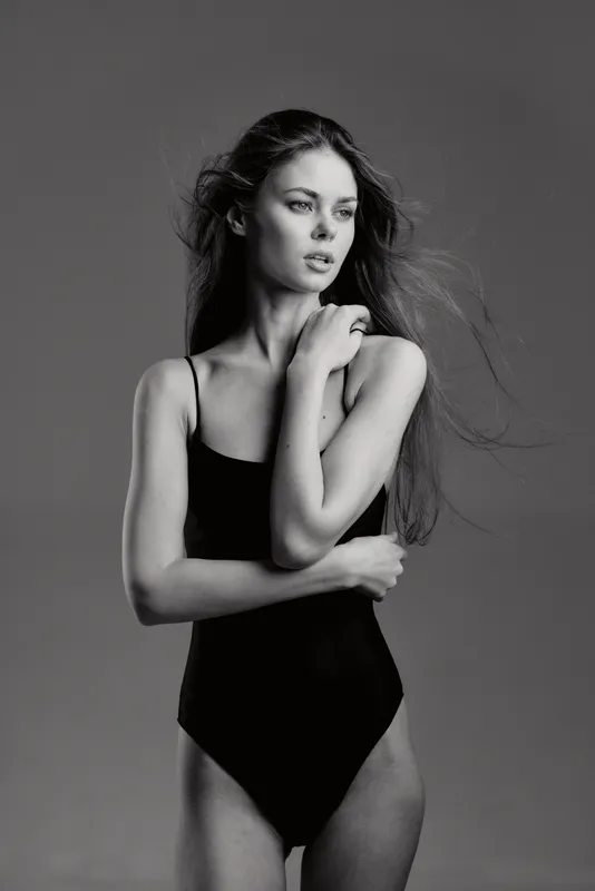 Black and white portrait of a thoughtful woman in a black bodysuit with long hair and natural pose.