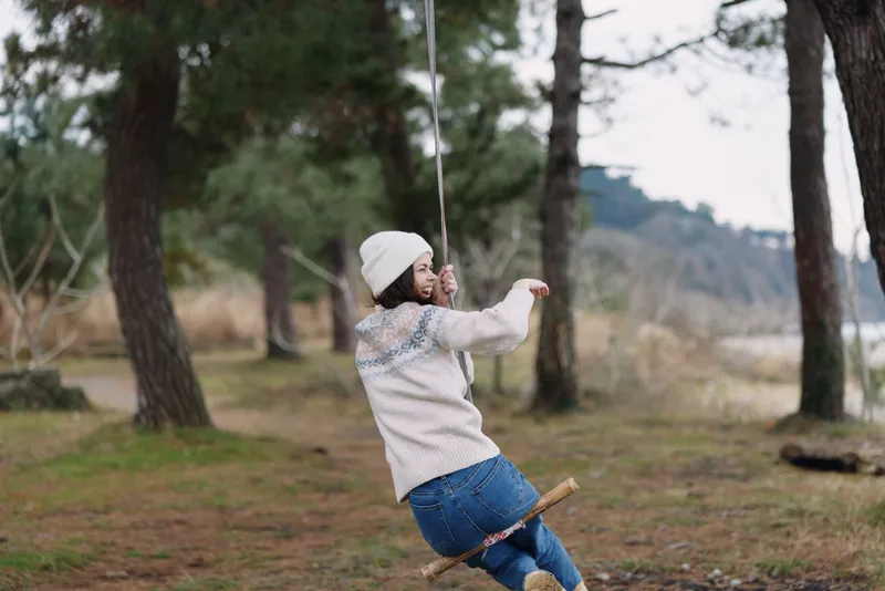 Swing, outdoor, nature, forest, play, joyful, woman, autumn, trees, landscape, casual scene of a woman on a wooden swing enjoying a carefree moment in a pine forest, wearing a sweater and hat amid