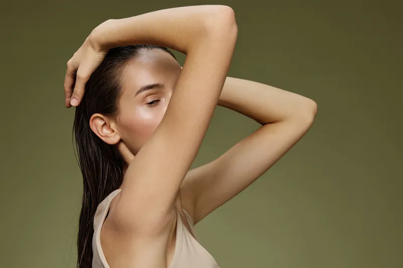 Elegant female model with neutral expression, showcasing healthy skin against a muted green background, embodying contemporary beauty and wellness concepts