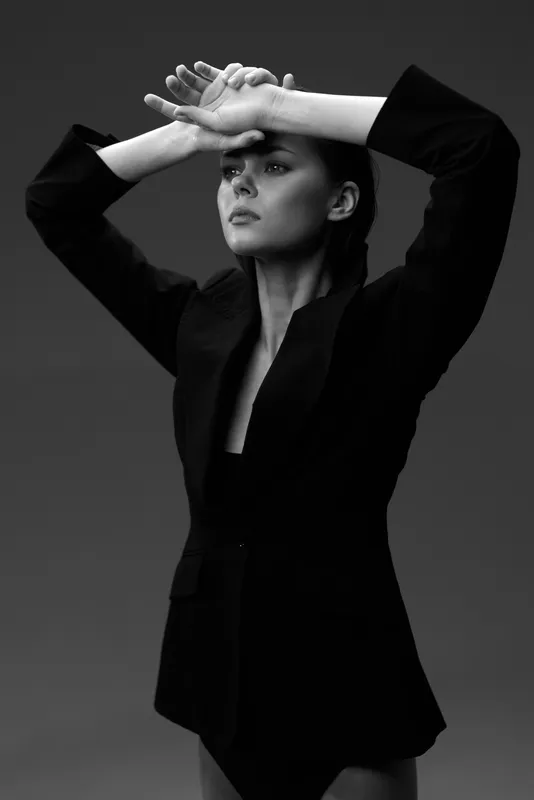 Black and white portrait of a woman in a blazer striking an elegant pose with hands near her face.