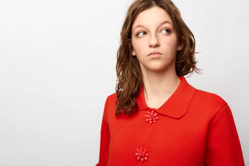 Young woman in red sweater looks to the side with a thoughtful expression. Studio portrait on white background. Concept of contemplation, emotion, and casual fashion.
