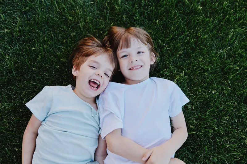 Happy children lying on green grass, enjoying a sunny day with playful smiles and cheerful expressions, creating a joyful outdoor atmosphere.