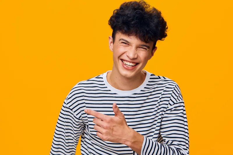 smiling man in striped shirt laughing joyfully against bright orange background, casual style, curly hair, cheerful expression, youthful energy