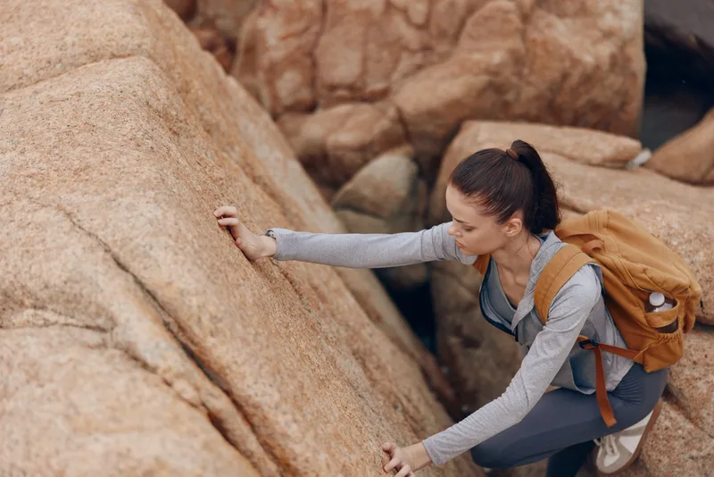 Young woman climbing rocky terrain, showcasing determination and adventure, dressed in casual athletic wear, with a focus on nature and outdoor exploration