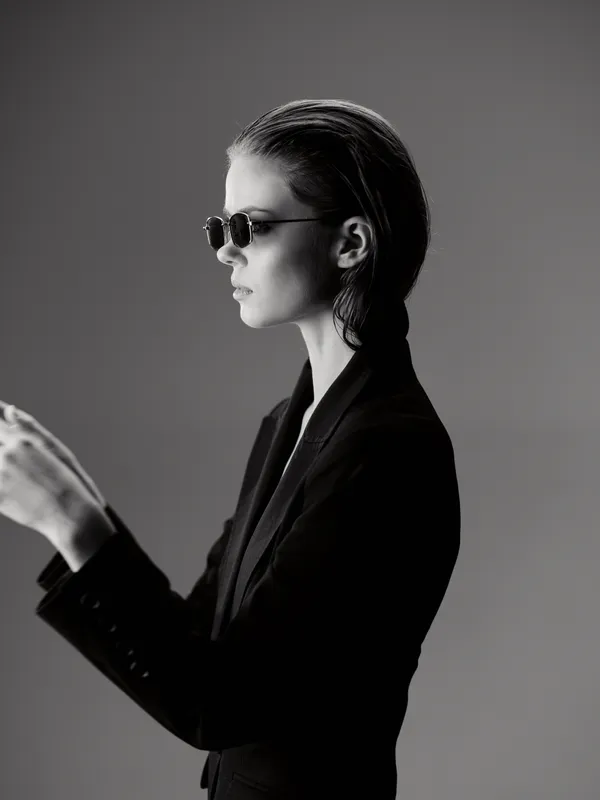 Black and white portrait of stylish woman wearing sunglasses and a suit jacket with slicked-back hair.