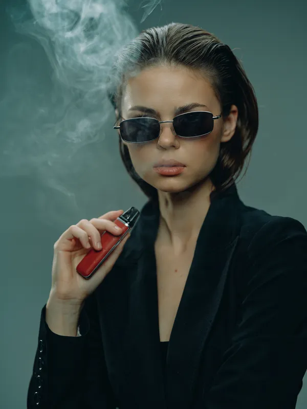 Stylish woman vaping in sunglasses with smoke, wearing black outfit, confident and modern lifestyle concept.