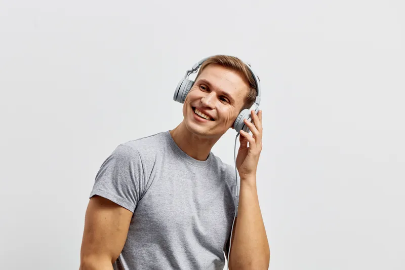 Smiling man with headphones enjoying music listen to audio device isolated on solid white background. Studio portrait of happy young male person wearing casual grey t-shirt. People lifestyle concept.