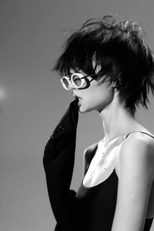 Black and white woman wearing white sunglasses and black outfit with messy short hair in stylish pose