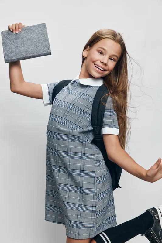 Girl in school uniform with backpack holding book and smiling, jumping and happy for education, youth and learning on white background studio. Child, teenager and study concept