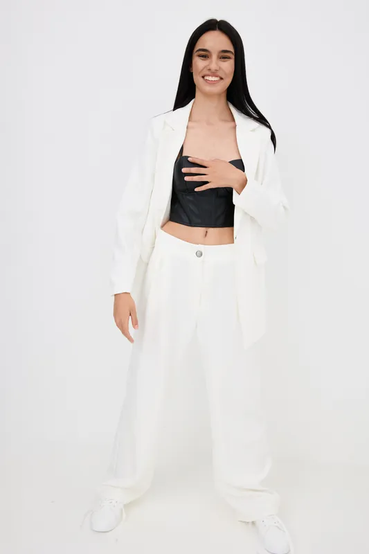 young woman wearing white suit and black crop top standing confidently with smile on white background, modern style and casual fashion outfit