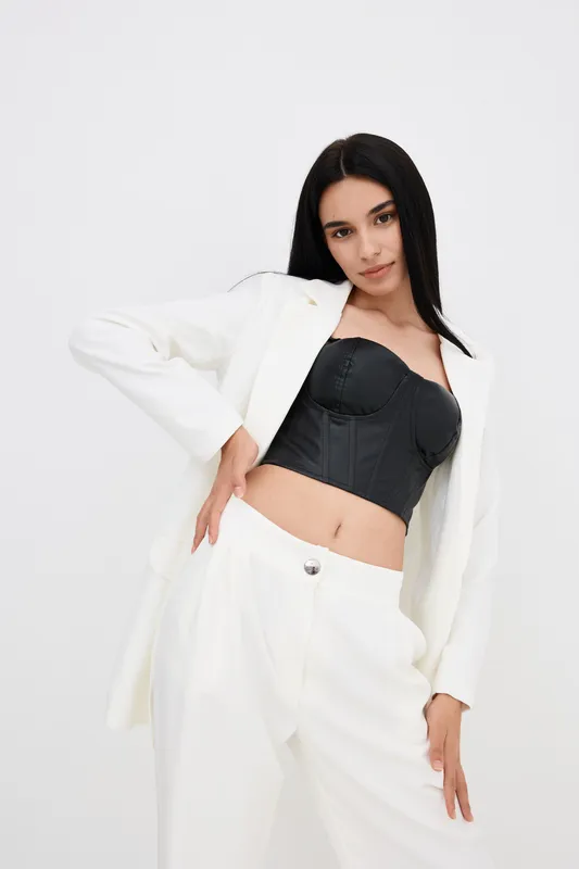 stylish woman in white suit and black corset poses confidently against white background, showcasing modern fashion with sleek straight hair and poised expression