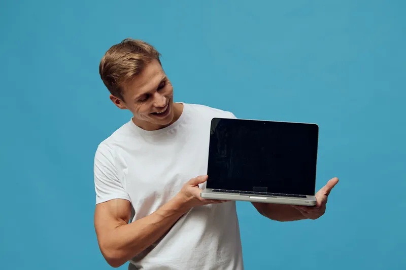 smiling man holding laptop showing blank screen in white t-shirt isolated on blue background digital nomad freelance work concept