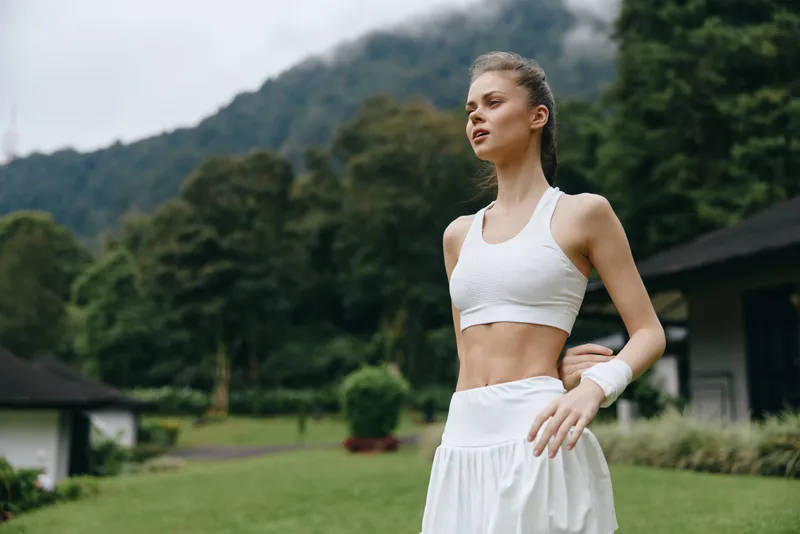 A young woman of Caucasian descent in athletic wear practicing yoga outdoors, radiating serenity and focus amidst lush green mountains, emphasizing healthy living and fitness