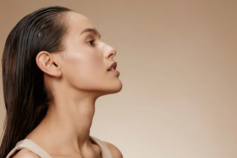 Profile of a serene young woman with long hair, showcasing natural beauty and glowing skin against a soft beige background, ideal for wellness and self care themes