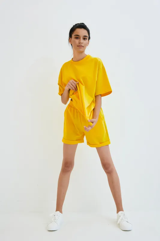 young woman wearing bright yellow casual outfit standing confidently against white background, minimalistic style, sporty look, comfortable summer wear, studio shot