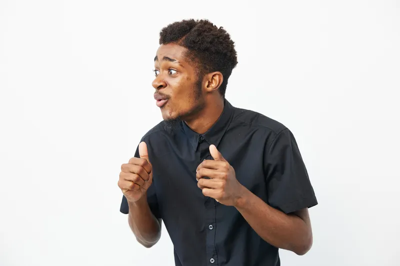 Enthusiastic African American man expressing excitement with gestures in a minimalist setting, showcasing dynamic emotions and engagement.