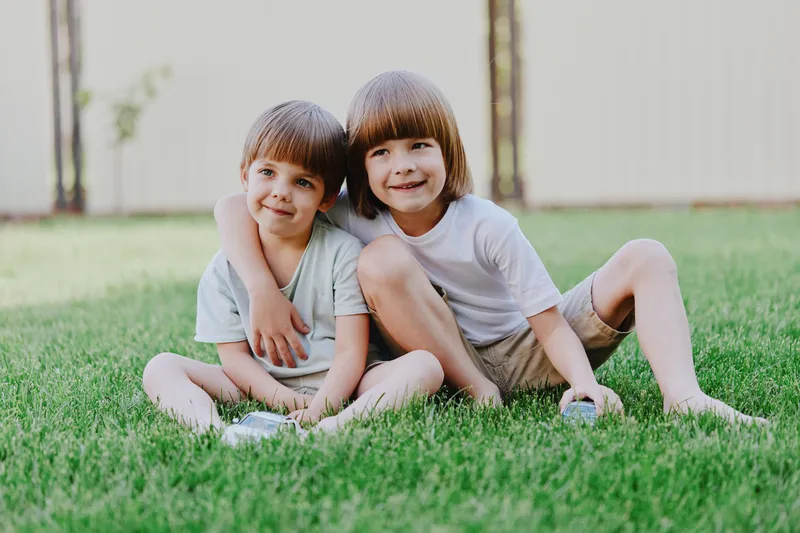 Caring children enjoying playful time outdoors, forming a strong bond while sitting on green grass, radiating happiness and innocence in a beautiful summer setting.