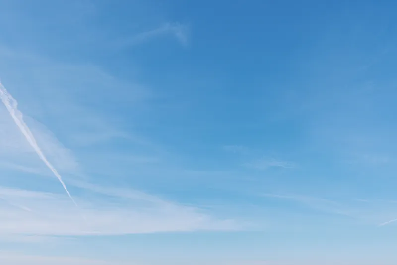 Blue sky with wispy clouds and a contrail across the horizon, conveying openness, serenity and fresh air in a minimalist landscape