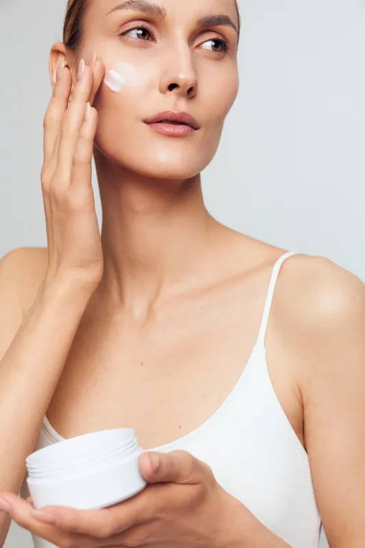 Woman applying face cream and moisturizer, holding a cosmetic jar, gentle skincare routine for beauty hygiene, smooth face care, calm spa self concept