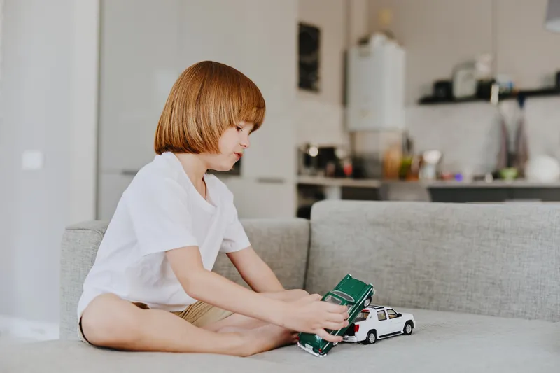 Joyful boy playing with toy cars on a cozy couch in a bright living room. A playful atmosphere highlighting childhood innocence and imagination.