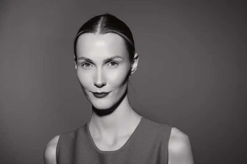 Portrait of a slim Caucasian woman with pale skin and slicked back hair wearing a sleeveless top against a plain dark background. Concept for beauty, fashion, and elegance.