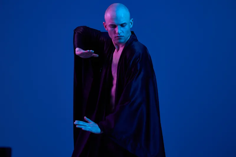 Dynamic man performing in a flowing black robe, showcasing graceful movements in a vivid blue light. Captivating and expressive atmosphere fills the image.