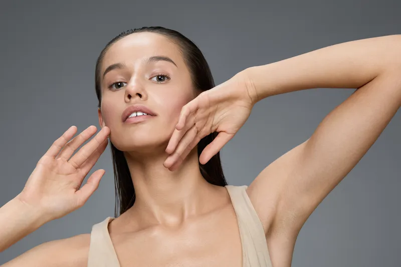 Young woman with flawless skin posing confidently, showcasing beauty and elegance against a minimalist gray background, perfect for lifestyle and wellness themes