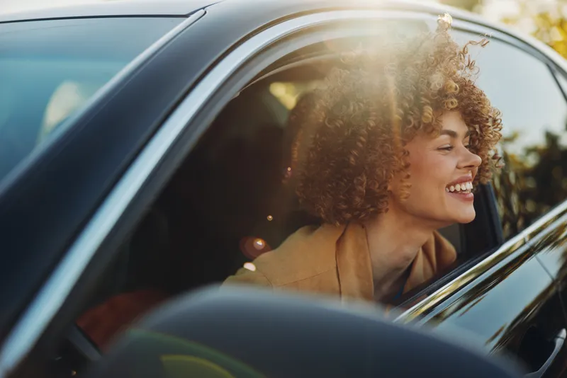 A joyful woman drives a car with sunlight streaming through the window, retro film tones add warm nostalgia, capturing a lifestyle portrait moment.