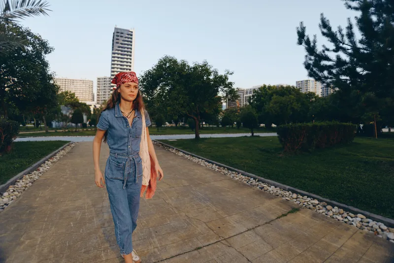 modern boho-western denim street style woman walking confidently outdoors with casual summer outfit and red bandana, film color tones in urban park setting