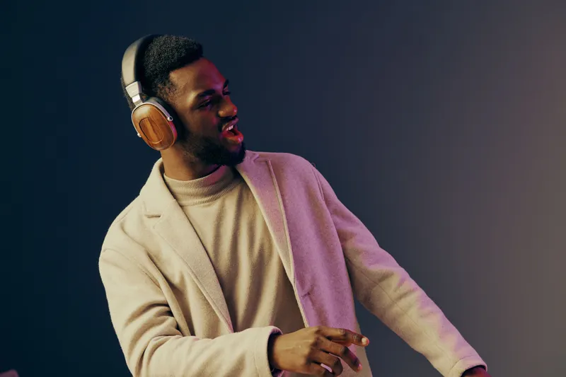 Stylish young Black man enjoying music with headphones, dressed in casual winter wear, expressing joy and relaxation against a gradient background