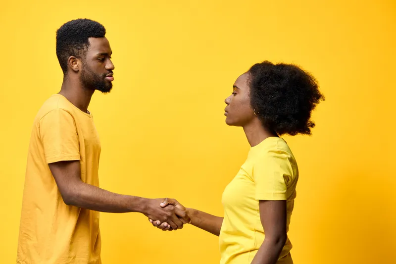 Two young African individuals shaking hands against a vibrant yellow background, symbolizing collaboration and unity in a bright, cheerful environment