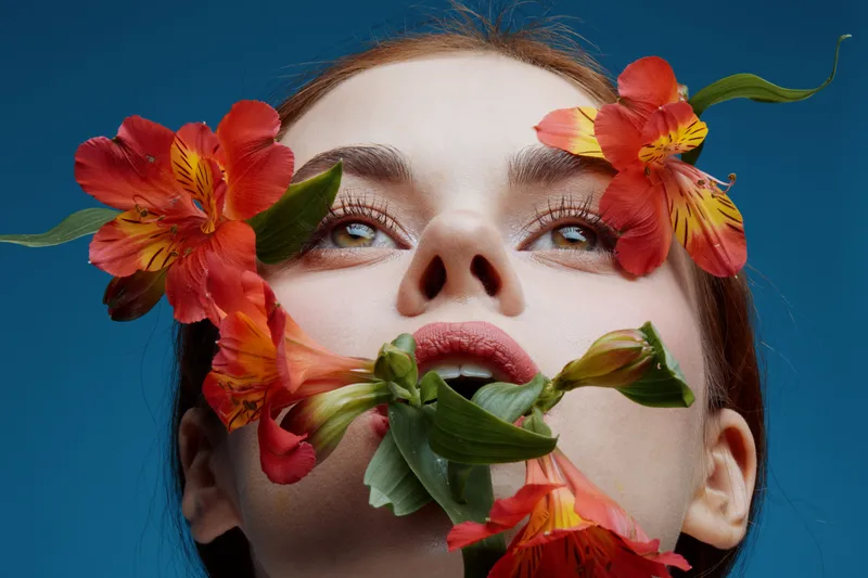 Female model with red flowers, blue background, showcasing beauty and nature, expressing tranquility and creativity Concept of natural beauty and floral inspiration