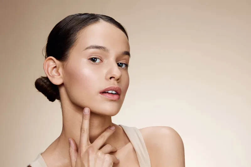 Close up portrait of a young woman with natural makeup showing a soft smile and healthy skin against a neutral background, highlighting beauty and skincare