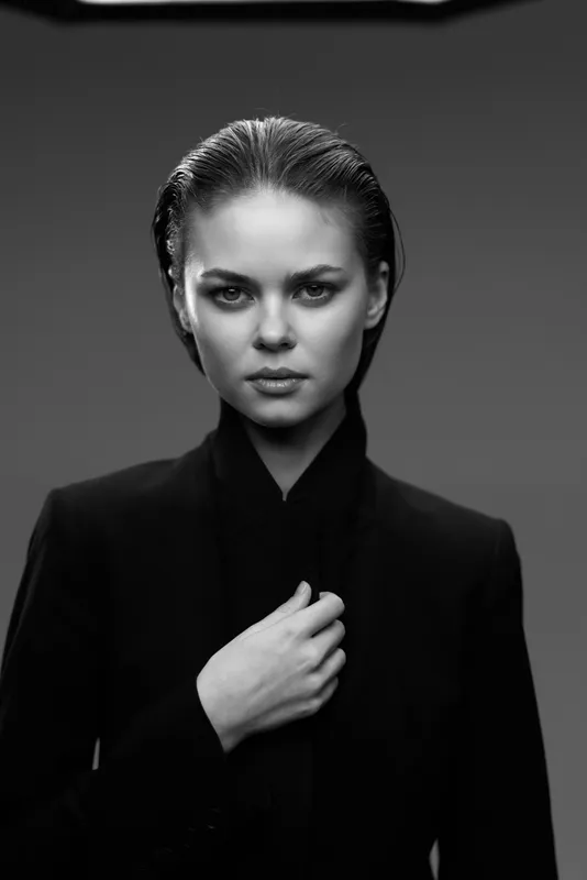 Black and white portrait of a serious woman with slicked-back hair wearing dark clothing and intense expression