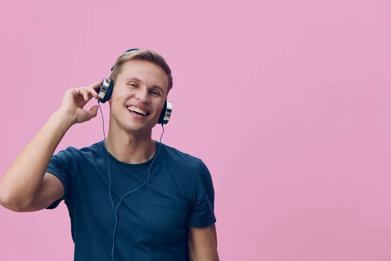 happy smiling young caucasian man listen music wear headphones casual t-shirt pink background studio portrait digital detox mental health concept
